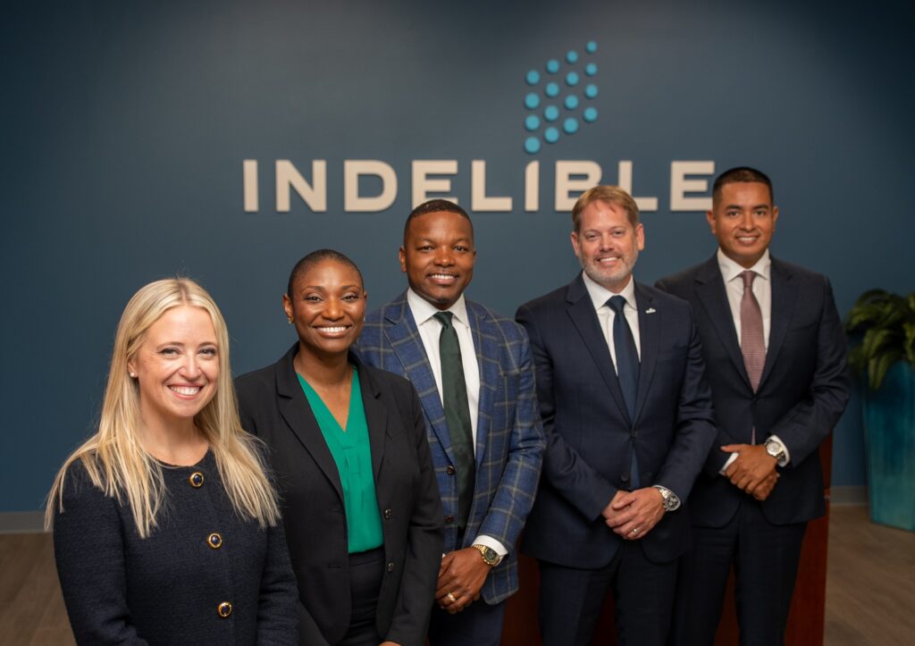 Five Indelible colleagues smiling together in front of the Indelible logo